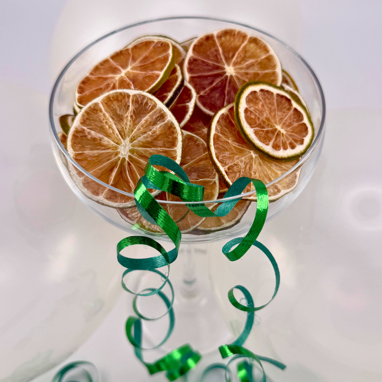 Dried citrus slices in a glass with green ribbons on a white background